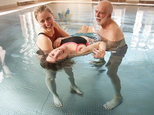 Zwei TherapeutInnen unterstützen eine liegende Person im Schwimmbecken