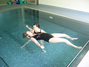Eine TherapeutIn unterstützt eine im Wasser liegende Person